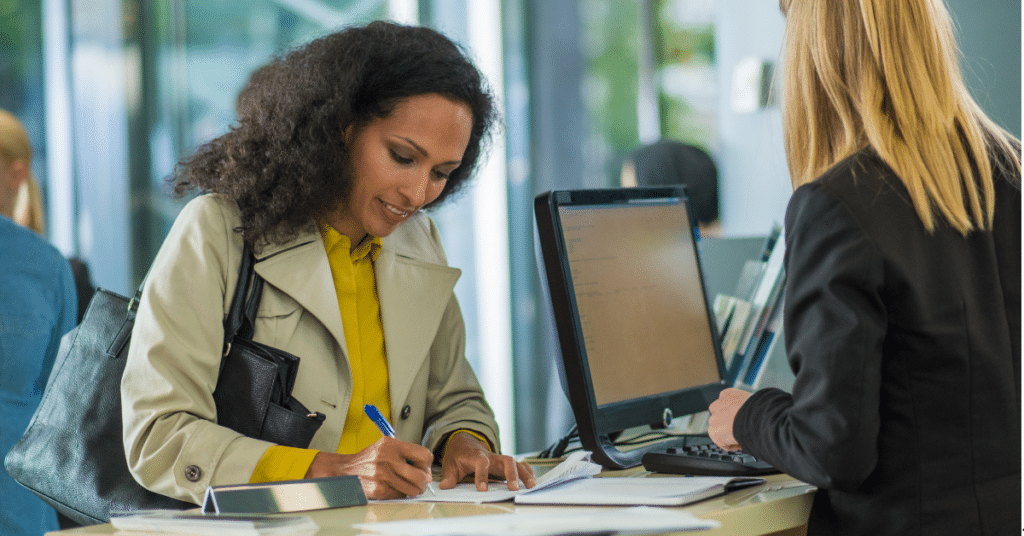 a credit union teller sitting behind a counter with a member signing a document at the counter