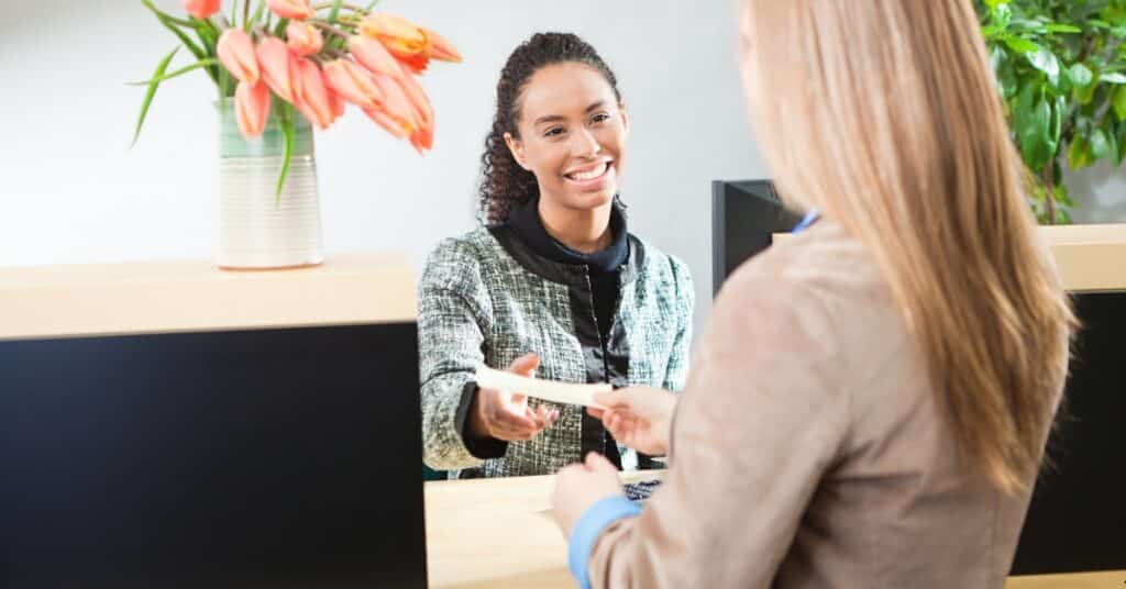 A smiling bank teller hands a commercial lending document to a customer across the counter.