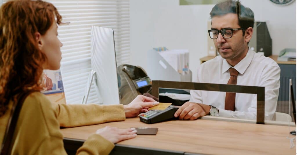 A person is handing a credit card to a bank teller to make a payment through a card reader.