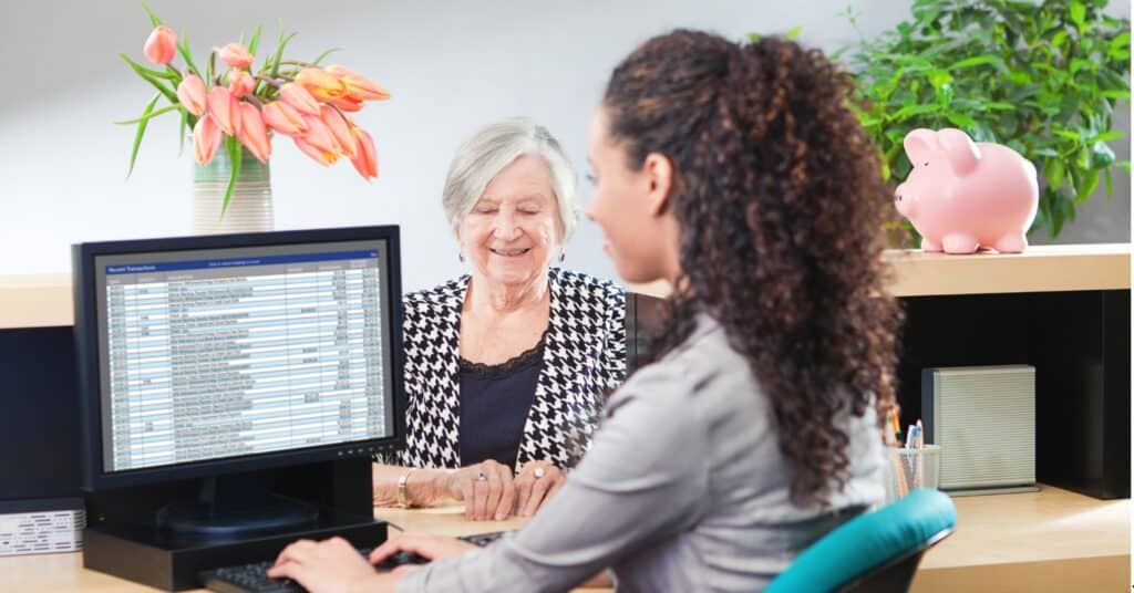 A credit union teller assists a customer at a desk with a computer.