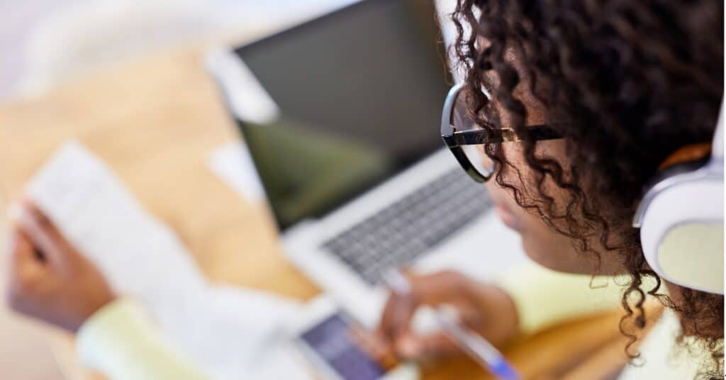 A person wearing headphones and glasses, looking over an electronic receipt at a laptop.