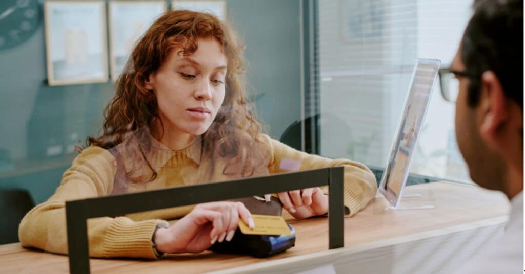 A person swipes a credit card on a payment terminal at a counter while another person looks on.